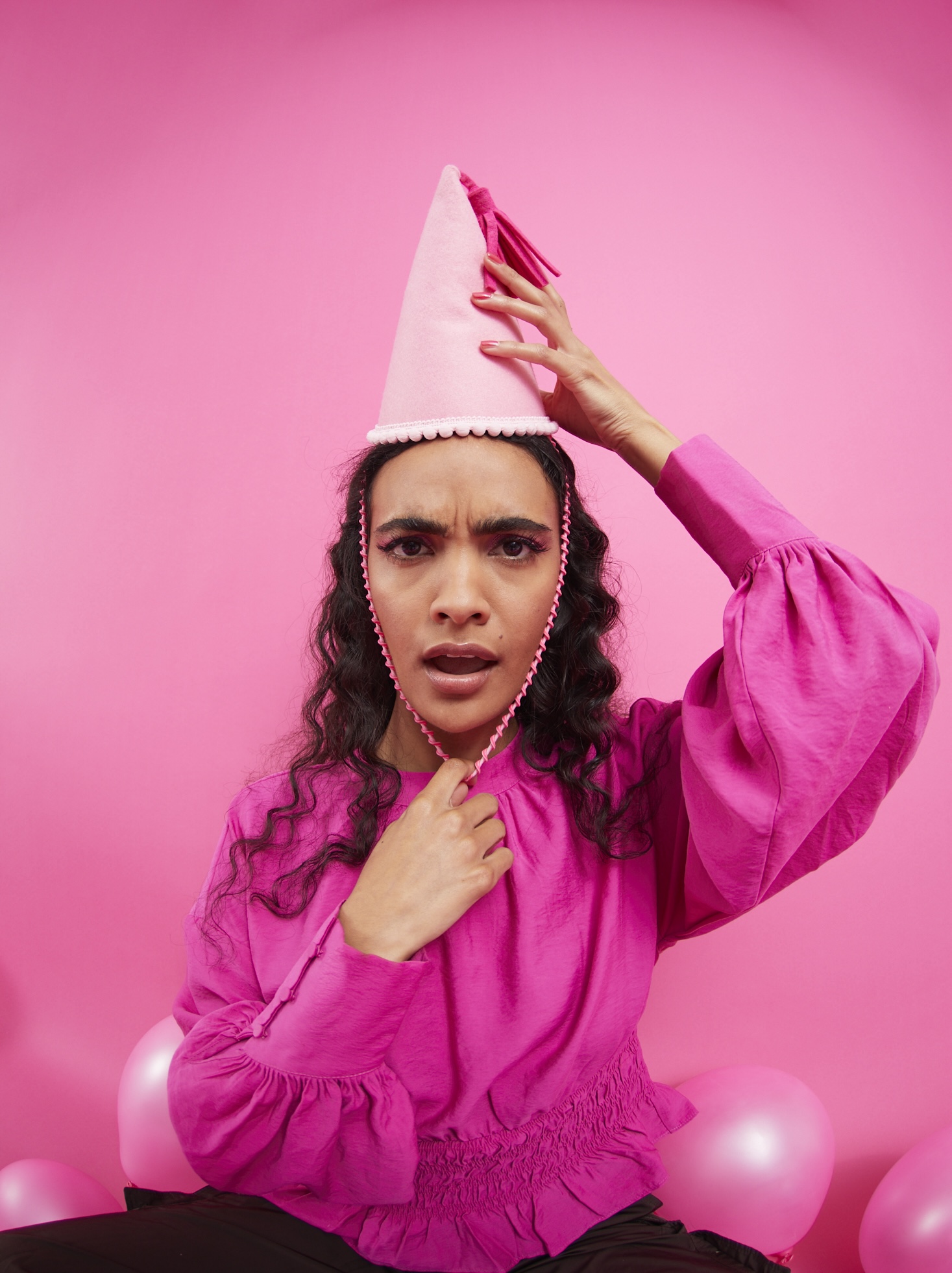 A woman in pink holds a party hat on her head